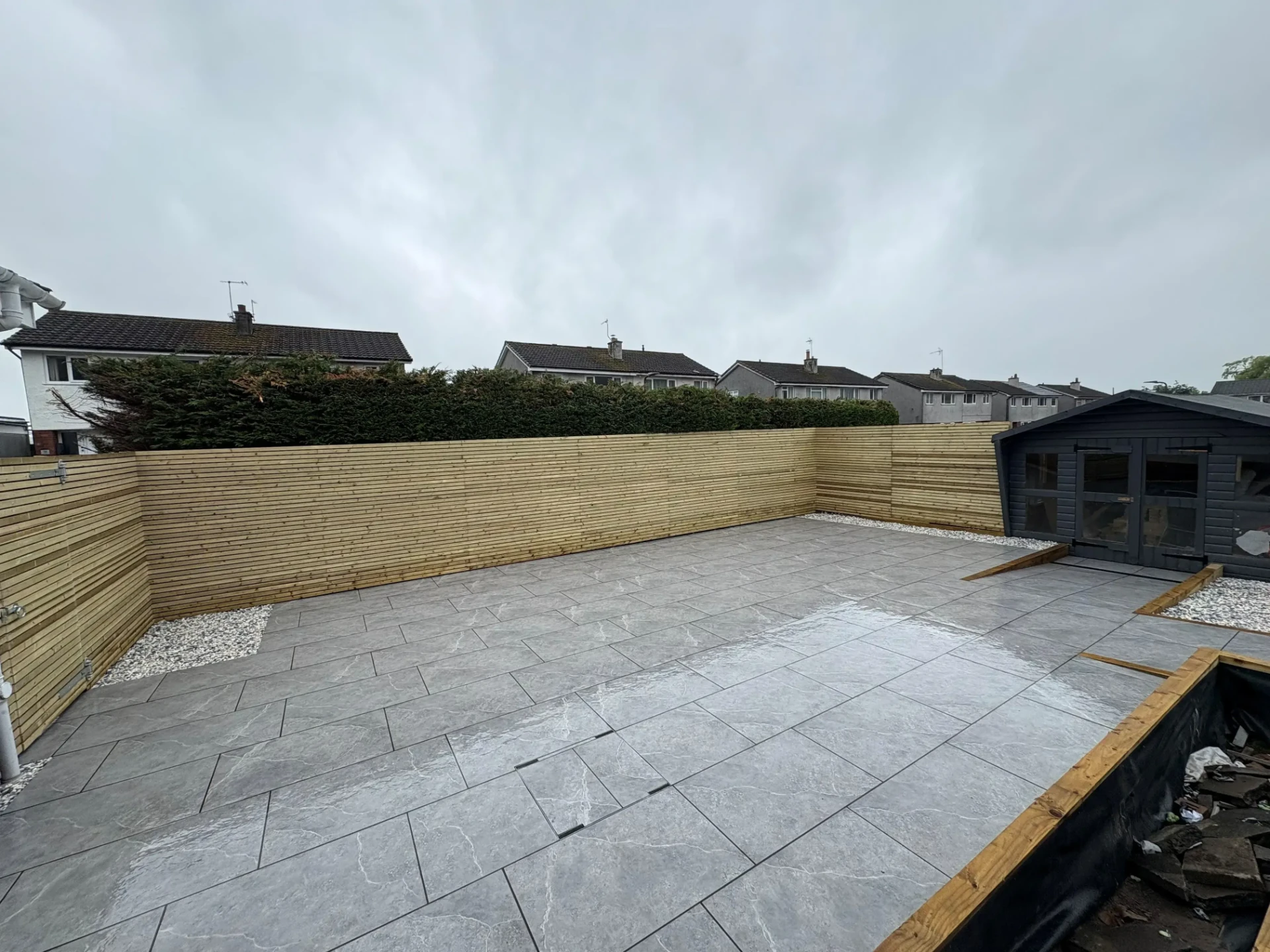 Horizontal slatted timber fencing around a newly paved rear garden with a summer house