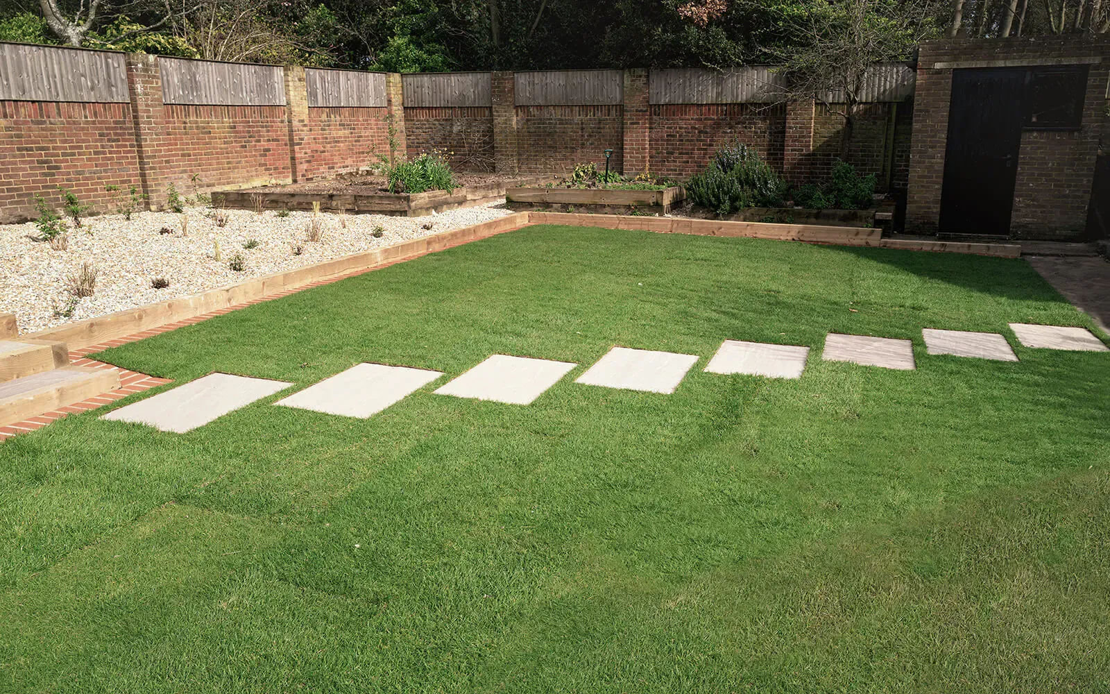 Freshly planted border with brick edging alongside a new lawn