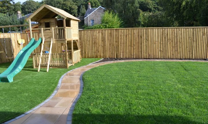 Feather edge board fencing enclosing a lawn with a children's playhouse and paved path
