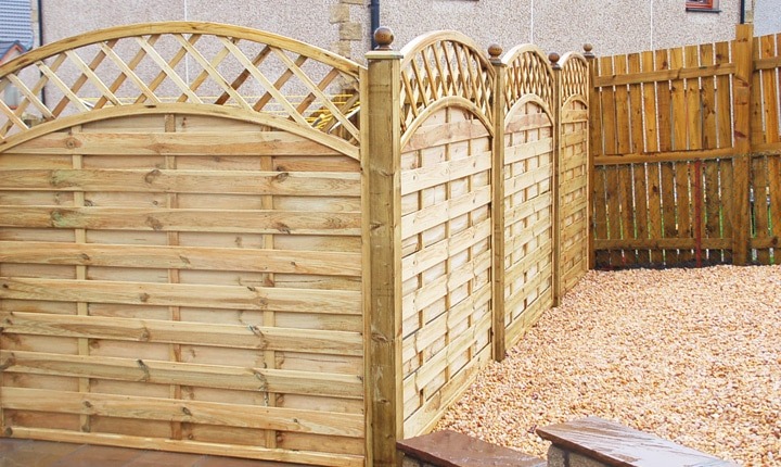 Curved top woven panel fencing with trellis tops beside a gravelled area